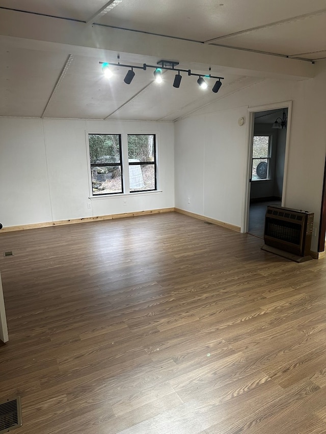 unfurnished room featuring hardwood / wood-style flooring, lofted ceiling, heating unit, and track lighting