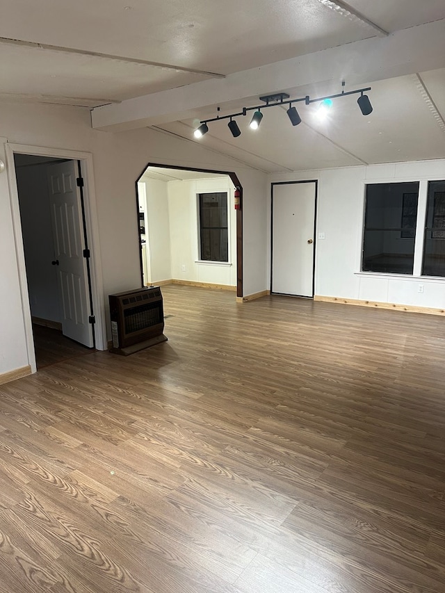 empty room featuring heating unit, track lighting, baseboards, and wood finished floors