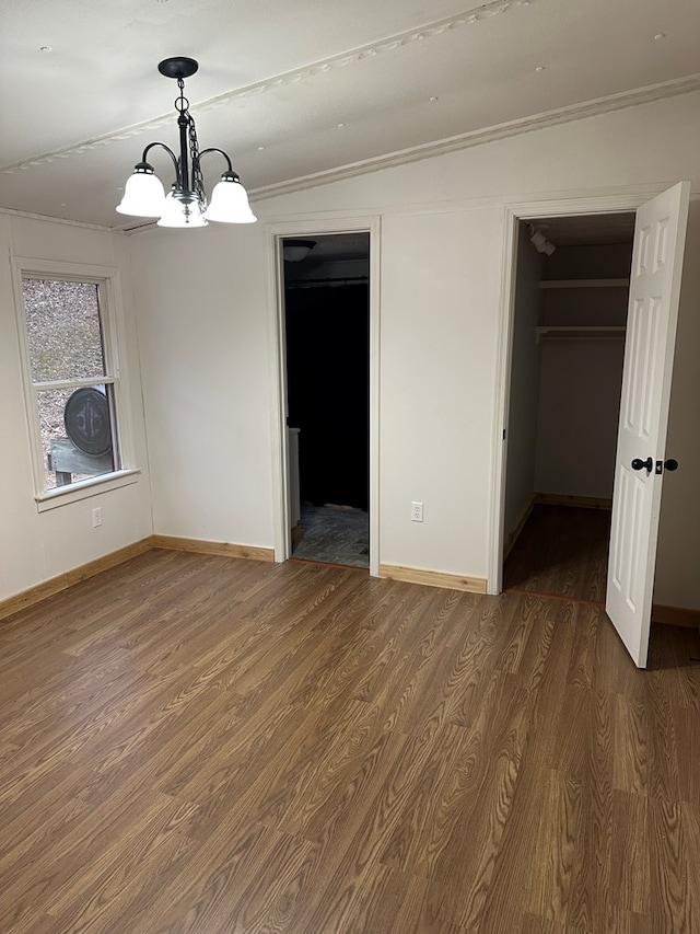 unfurnished bedroom with a walk in closet, crown molding, wood finished floors, and baseboards