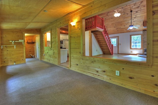 unfurnished living room featuring wooden walls, lofted ceiling, stairway, carpet, and wood ceiling