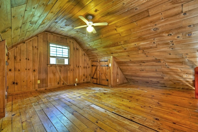 additional living space with hardwood / wood-style floors, lofted ceiling, cooling unit, ceiling fan, and wooden walls