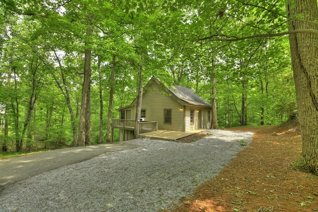 view of home's exterior with a deck, driveway, and a wooded view