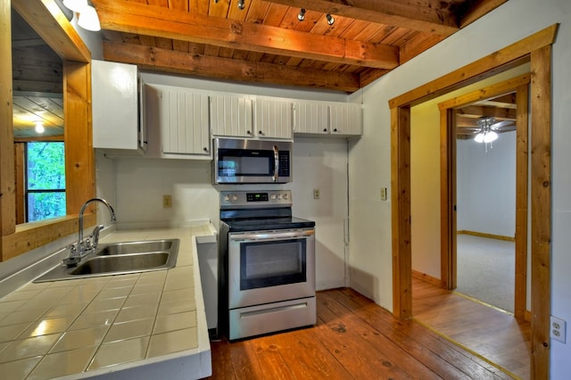 kitchen with stainless steel appliances, tile counters, a sink, wooden ceiling with exposed beams, and hardwood / wood-style flooring