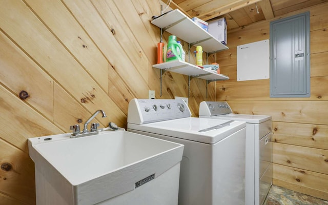 clothes washing area with washing machine and dryer, sink, electric panel, and wooden walls