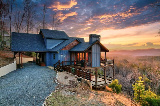 view of front of home with driveway, a wooden deck, roof with shingles, a chimney, and board and batten siding