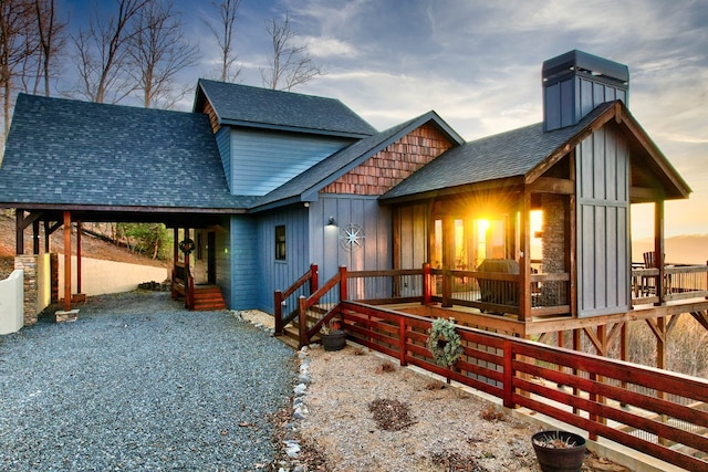 view of front facade with a shingled roof, gravel driveway, board and batten siding, and a chimney