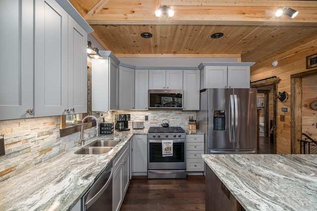 kitchen featuring wood walls, dark wood-type flooring, sink, appliances with stainless steel finishes, and light stone counters