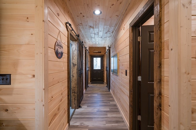 hallway featuring a barn door, dark hardwood / wood-style floors, wooden walls, and wood ceiling