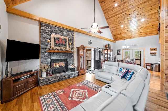 living room featuring a stone fireplace, light hardwood / wood-style flooring, high vaulted ceiling, and ceiling fan with notable chandelier