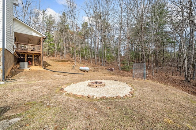 view of yard with central air condition unit, a deck, ceiling fan, and an outdoor fire pit