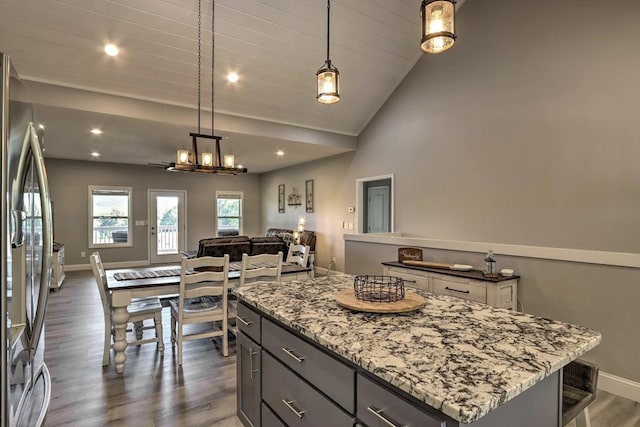 kitchen featuring light stone countertops, stainless steel fridge, dark hardwood / wood-style flooring, a center island, and hanging light fixtures