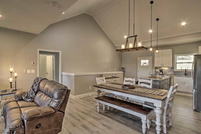 dining area with light hardwood / wood-style floors, high vaulted ceiling, and sink