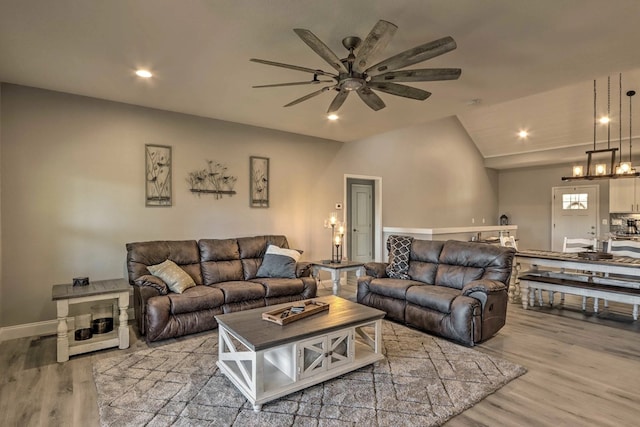 living room with ceiling fan, light hardwood / wood-style flooring, and vaulted ceiling