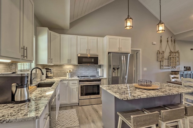 kitchen featuring appliances with stainless steel finishes, sink, decorative light fixtures, a center island, and white cabinetry