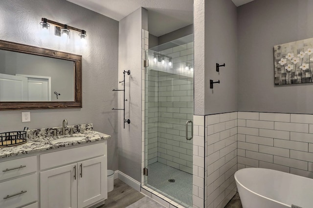 bathroom with plus walk in shower, vanity, hardwood / wood-style flooring, and tile walls