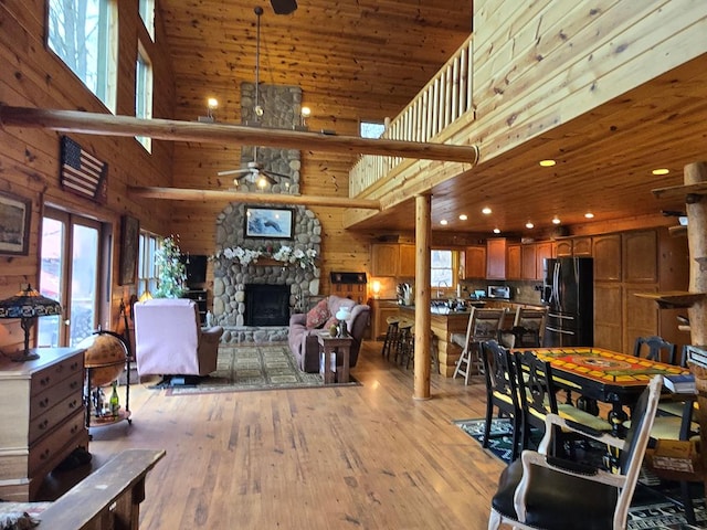 dining room with a stone fireplace, a towering ceiling, wood ceiling, ceiling fan, and light hardwood / wood-style floors