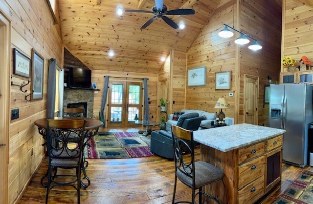 kitchen with wood walls, ceiling fan, stainless steel fridge, and hardwood / wood-style flooring