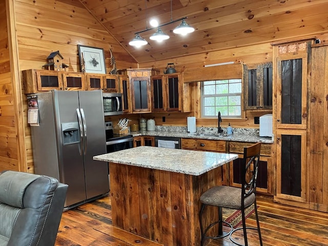 kitchen with stainless steel appliances, wood walls, dark wood-style floors, and a sink