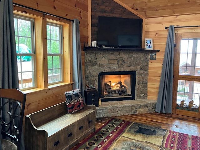 living area with wood walls, a stone fireplace, wood-type flooring, and lofted ceiling