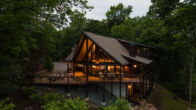 back of property featuring a forest view, roof with shingles, and a wooden deck