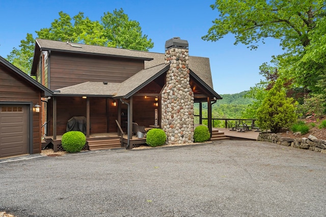 rustic home featuring a porch, a shingled roof, and a chimney