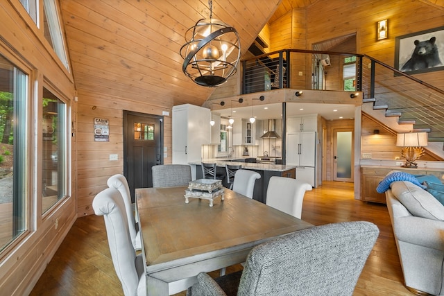 dining room featuring an inviting chandelier, wooden walls, high vaulted ceiling, wood finished floors, and stairway