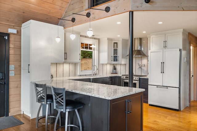 kitchen featuring stainless steel range with gas cooktop, a peninsula, a sink, paneled refrigerator, and white cabinets