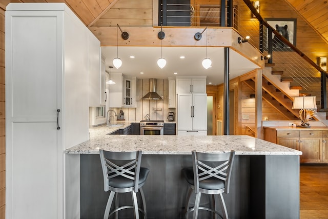 kitchen with a sink, white cabinetry, a peninsula, wall chimney range hood, and dark wood-style floors