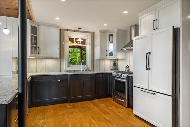 kitchen with light wood finished floors, high end fridge, gas range, wall chimney range hood, and tasteful backsplash
