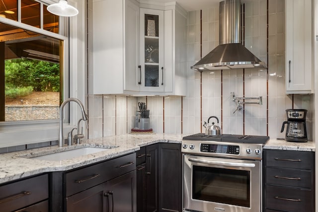 kitchen featuring a sink, wall chimney exhaust hood, gas stove, white cabinetry, and decorative backsplash