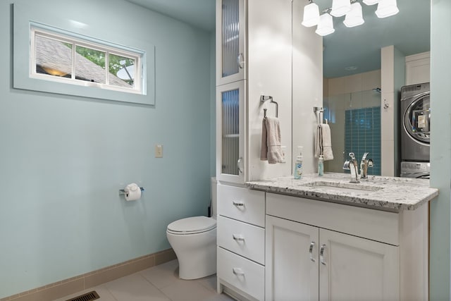 full bathroom with toilet, stacked washer and dryer, tile patterned floors, baseboards, and vanity