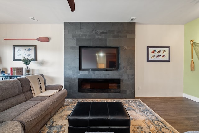 living room with a tiled fireplace, visible vents, wood finished floors, and baseboards