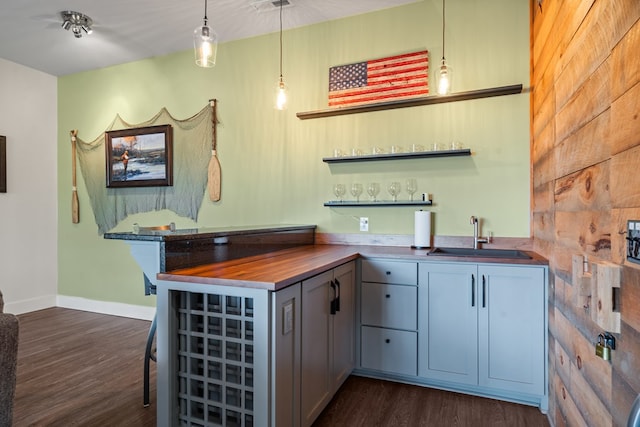 bar featuring decorative light fixtures, baseboards, a sink, wet bar, and dark wood-type flooring
