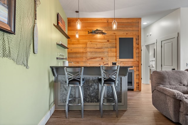 kitchen with decorative light fixtures, baseboards, open floor plan, a kitchen breakfast bar, and wood finished floors