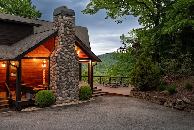 view of property exterior featuring roof with shingles, a chimney, and a wooden deck