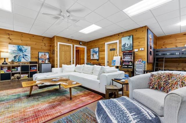 living room with a drop ceiling, wooden walls, and ceiling fan