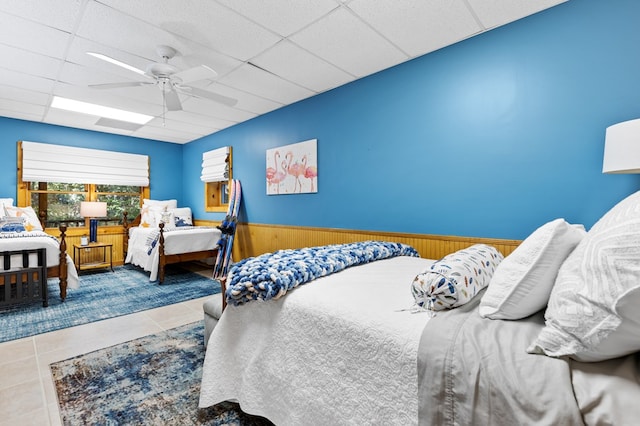 bedroom with a paneled ceiling, wood walls, ceiling fan, and tile patterned floors