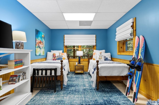 bedroom featuring a drop ceiling, wood walls, and dark tile patterned floors