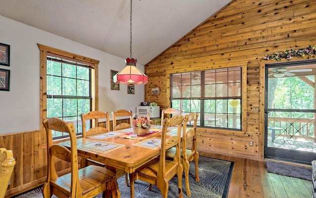 dining space featuring ceiling fan, a healthy amount of sunlight, wood-type flooring, lofted ceiling, and wood walls