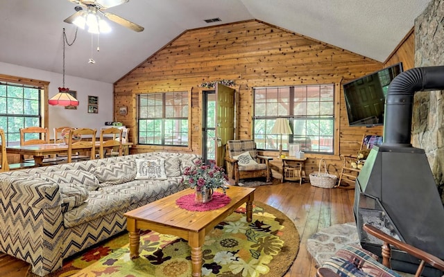 living room with ceiling fan, hardwood / wood-style floors, a wood stove, lofted ceiling, and wood walls