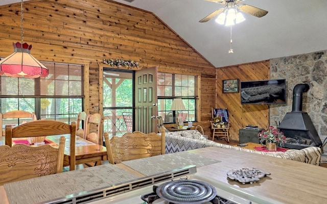 dining room featuring a wood stove, a wealth of natural light, lofted ceiling, and wood walls