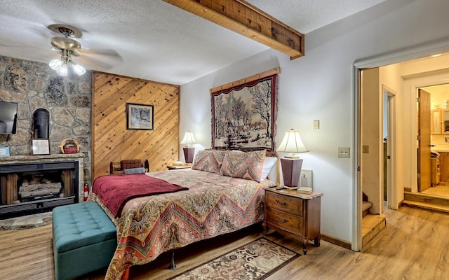 bedroom with a textured ceiling, ceiling fan, beam ceiling, light hardwood / wood-style floors, and wood walls