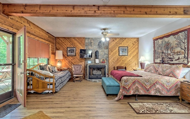 bedroom with hardwood / wood-style floors, wood walls, a wood stove, ceiling fan, and a textured ceiling