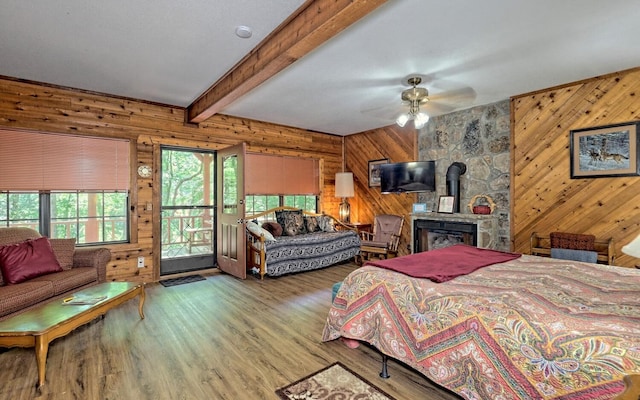 bedroom featuring light wood-type flooring, access to outside, ceiling fan, beamed ceiling, and a wood stove