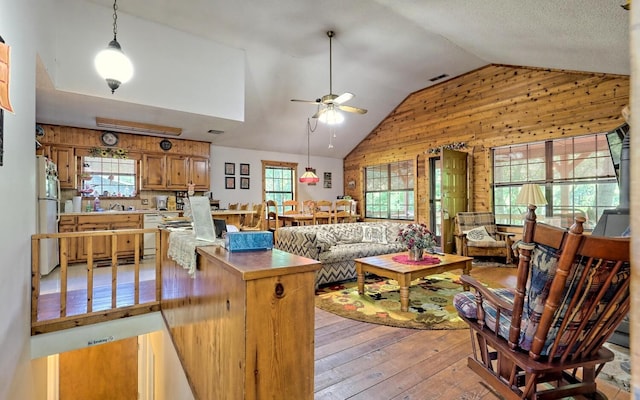 living room with a wealth of natural light, wood walls, light hardwood / wood-style flooring, and ceiling fan