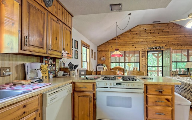 kitchen featuring kitchen peninsula, vaulted ceiling, decorative light fixtures, white appliances, and wooden walls