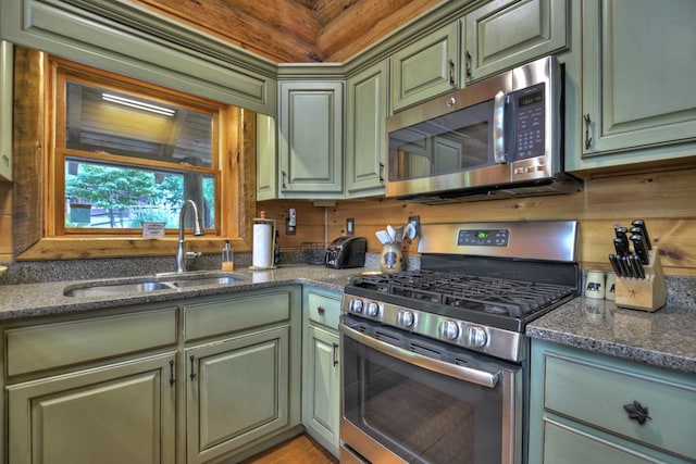 kitchen featuring green cabinets, appliances with stainless steel finishes, dark stone counters, and sink