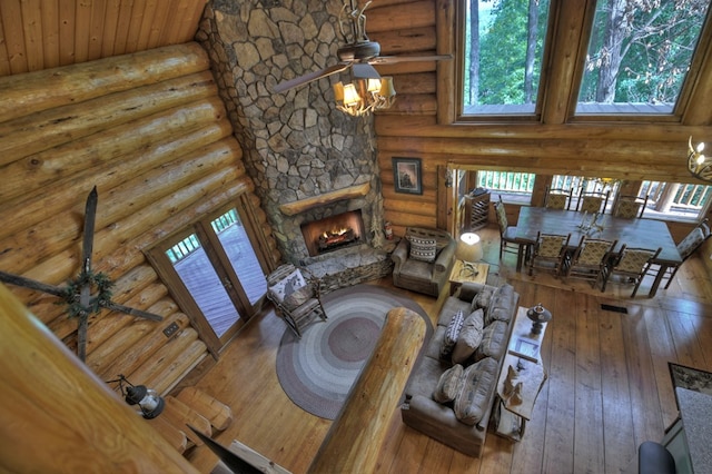 living room with a high ceiling, hardwood / wood-style floors, a stone fireplace, rustic walls, and ceiling fan