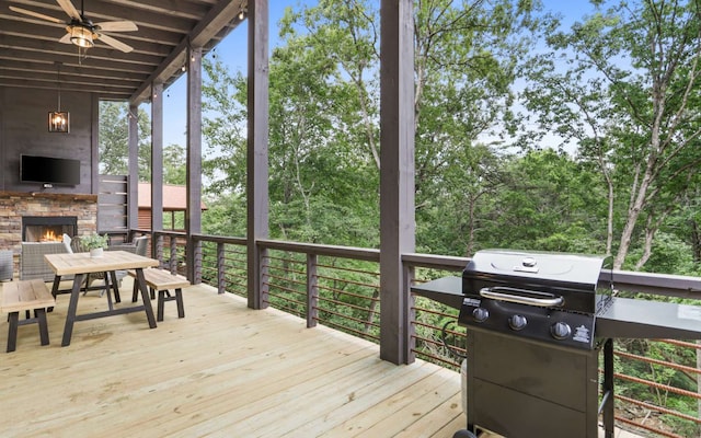 wooden deck featuring an outdoor stone fireplace, area for grilling, and ceiling fan