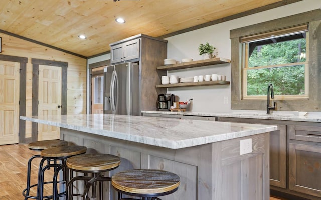 kitchen with a breakfast bar, lofted ceiling, stainless steel refrigerator with ice dispenser, light wood-type flooring, and light stone counters